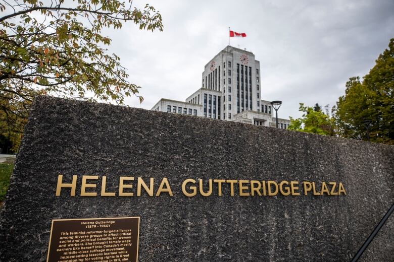 A sign on a wall that reads 'Helena Gutteridge Plaza', with Vancouver City Hall visible in the background.