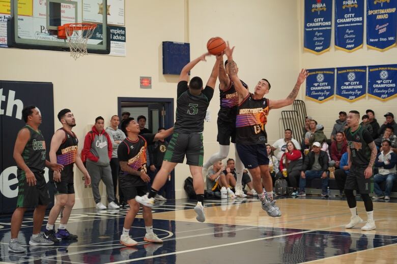 Three basketball players leap for the ball as other team members watch in anticipation