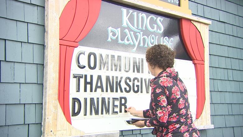 A woman adds lettering to a sign on the side of a building.