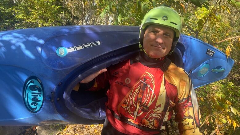 A man stands in water gear and a kayak on a shoreline.