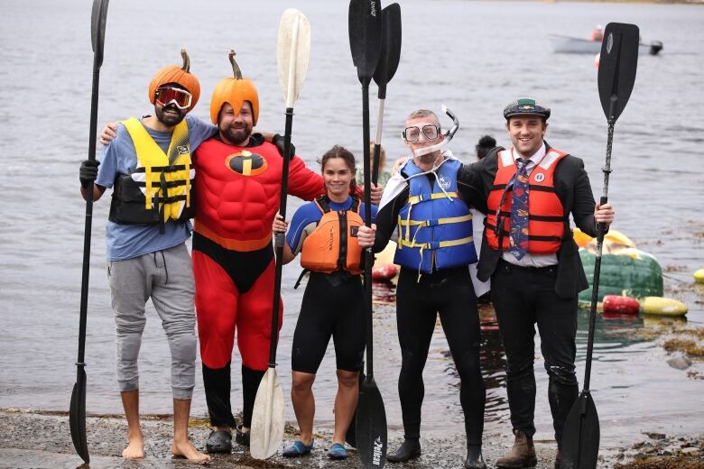 Five pumpkin racers dressed in wetsuits stand side-by-side at the edge of the water.