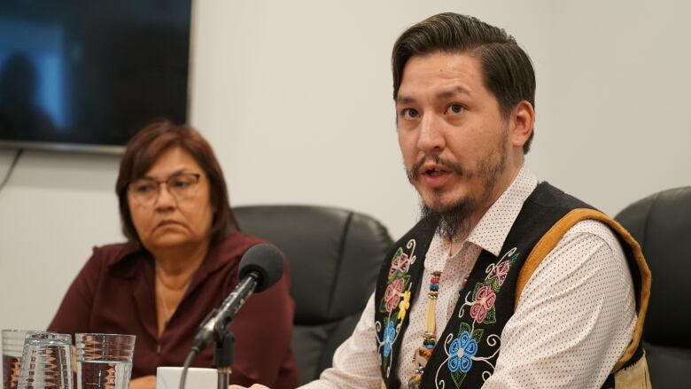 A man sits at a table before a microphone.