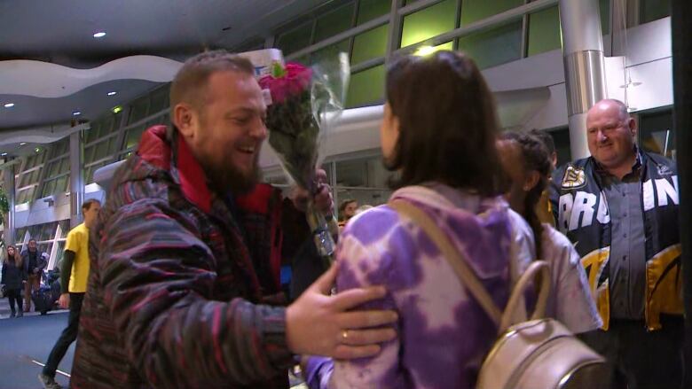 A man hugs his family with a large smile on his face.