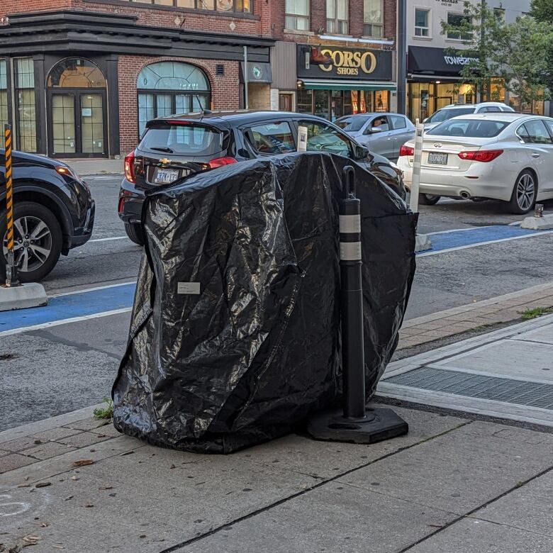 A public garbage bin covered in a black tarp.