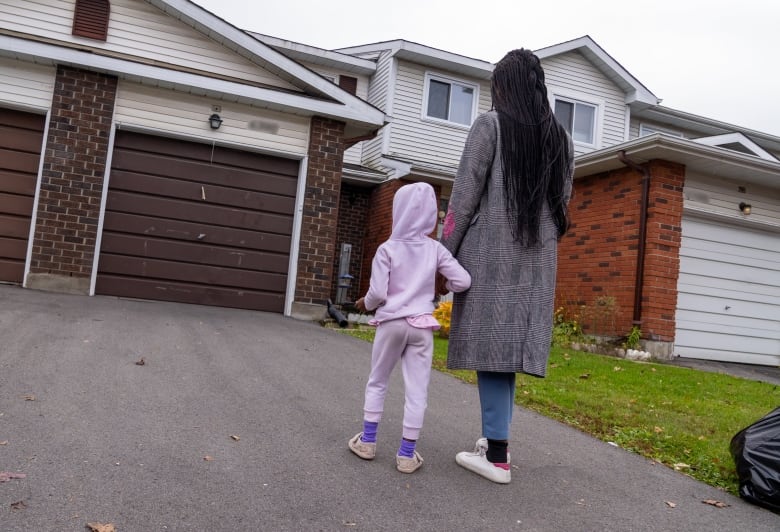 A woman and a child hold hands looking at a townhome.