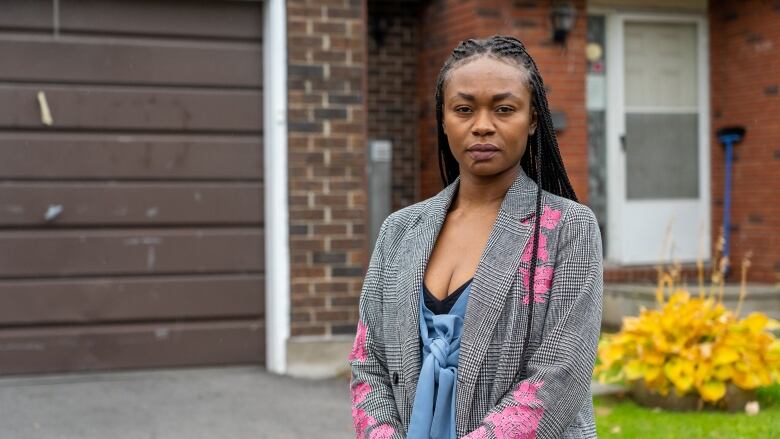 A woman stands on a driveway of a home looking at the camera.