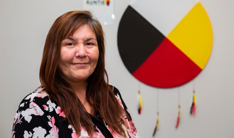 An older Indigenous women smiles standing in front of a medicine wheel.