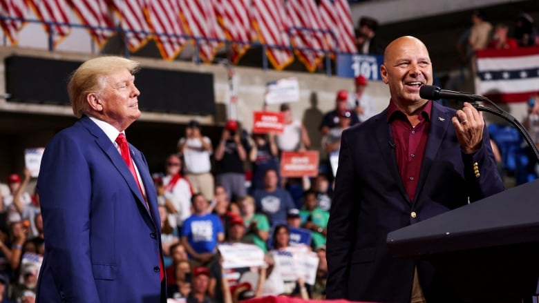 Two men stand at a rally holding microphones.