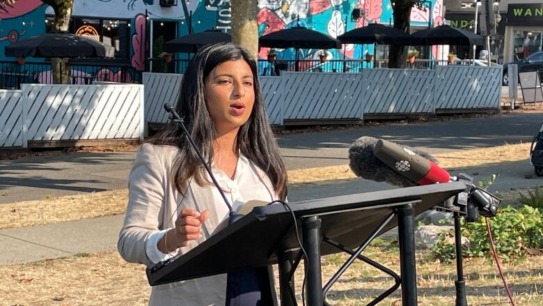 B.C. NDP leadership candidate Anjali Appadurai speaks in front of a podium in a light-coloured blazer and a white shirt.