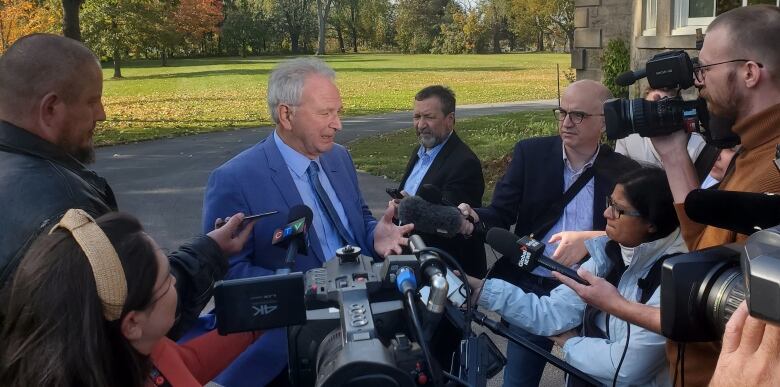 Man in a blue suit surrounded by cameras and reporters. 