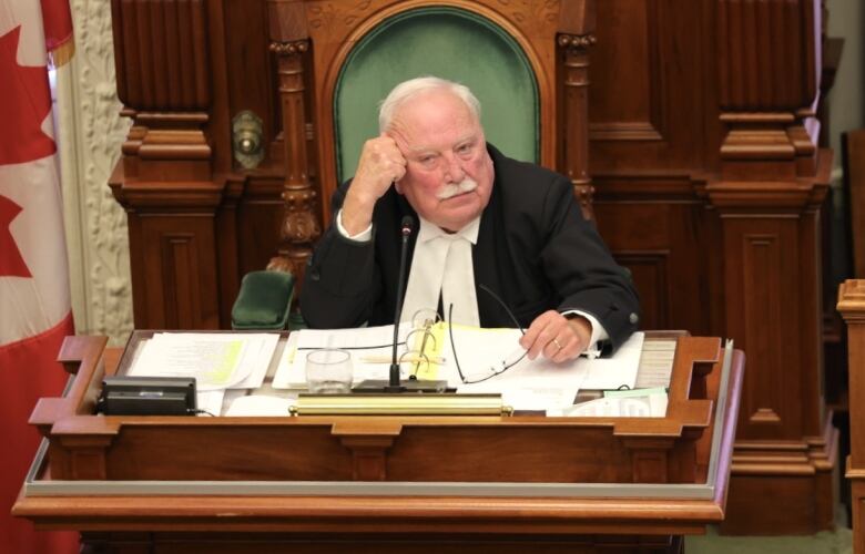 A man with white hair wearing black robes sits behind a wooden desk at the Nova Scotia legislature.