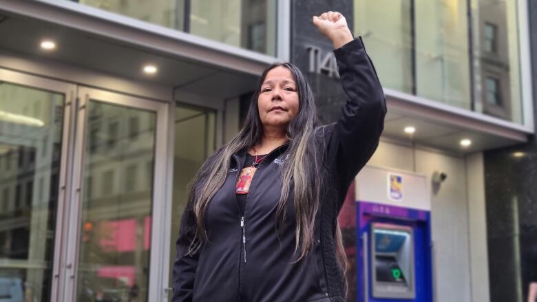 Kukpi7 (Chief) Judy Wilson of the Skatsin te Secwepemc-Neskonlith Indian Band raises her fist outside in downtown Montreal, standing in front of an RBC sign.