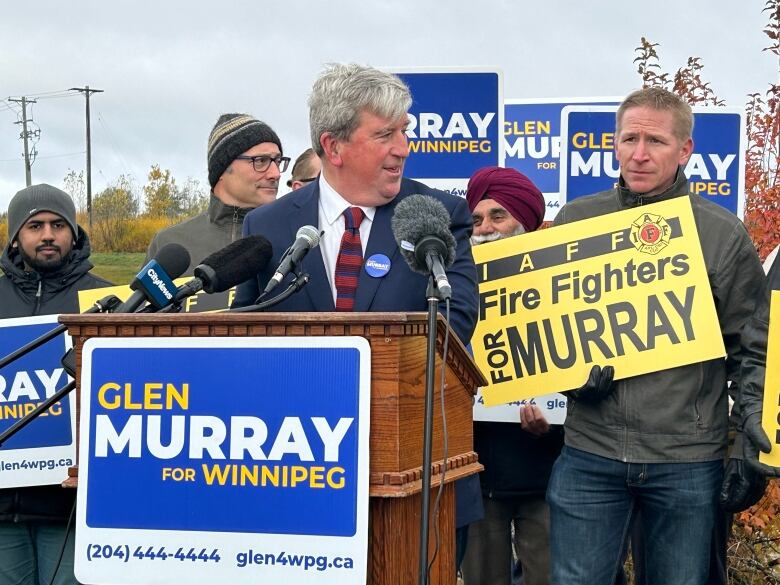 A man wearing a suit is speaking at a podium with a sign saying 