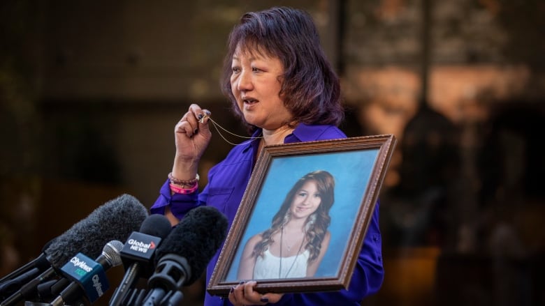 A woman holds up her locket as she carries a picture of a child.