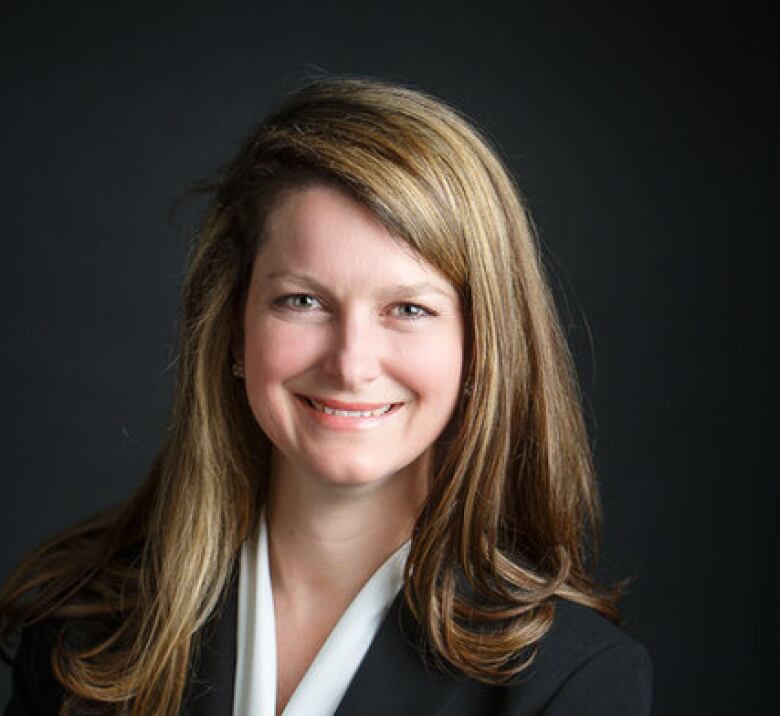 Portrait of a woman smiling, wearing black with black background.