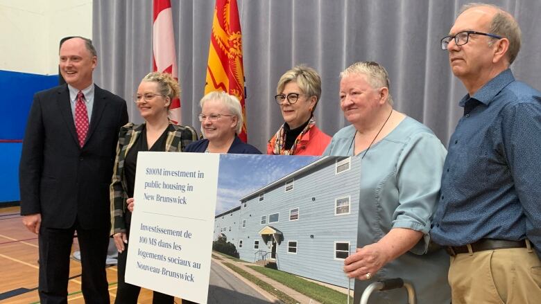 Six people standing in a row, holding a large sign with a picture of a town-house-style development. 