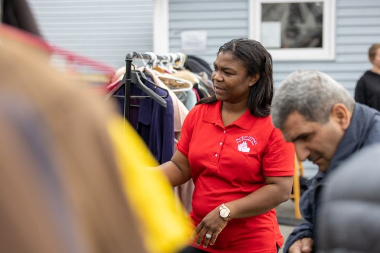 a woman wears a red shirt stands near a rack of clothing.