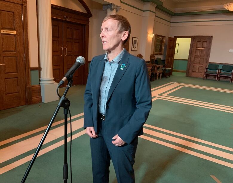 A person in a suit stands speaking into a microphone.