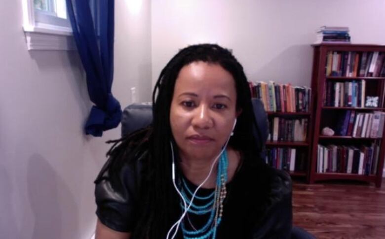 A Black woman with dark locs in front of a book shelf