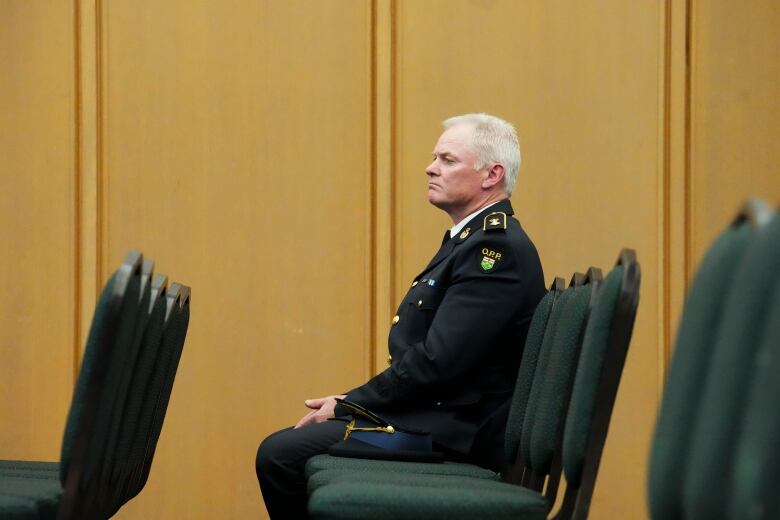 A police officer in uniform sits in a chair, surrounded by empty chairs.