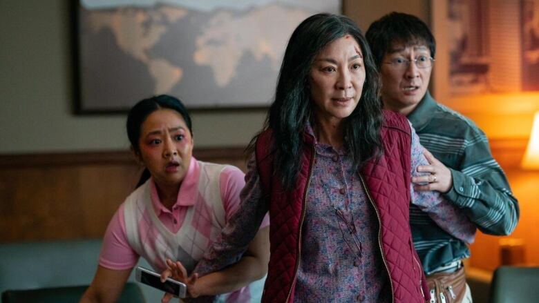 A still frame from the film Everything Everywhere All at Once. Stephanie Hsu, Michelle Yeoh and Ke Huy Quan looking alarmed at something off camera.