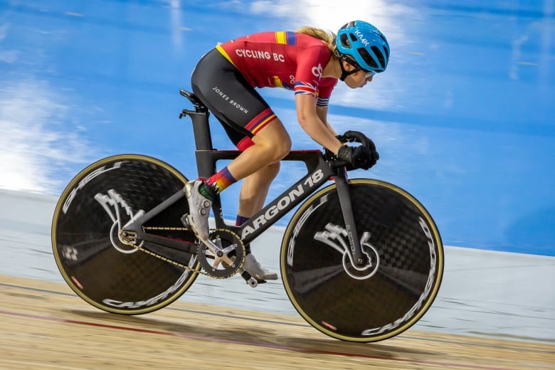 A woman wearing red and gold and a blue helmet speeds around a track.