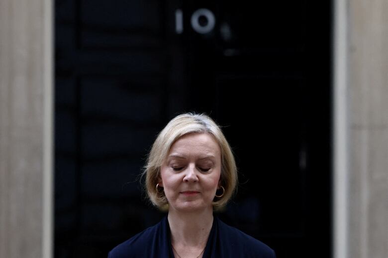 A woman with blonde hair looks down as she stands in front of a door marked with the number 10.