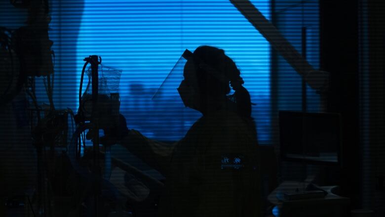 A nurse backlit against an evening or early morning sky sorts through the IV fluids and tubes for a patient. 