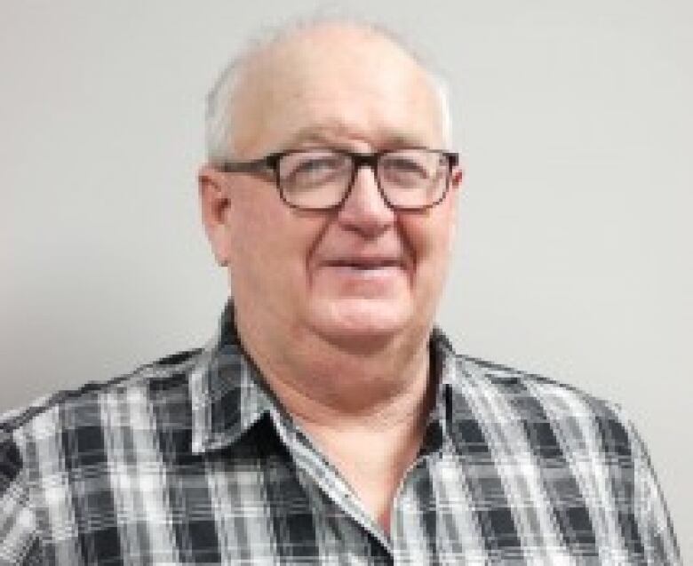 A man with white hair and glasses smiles.