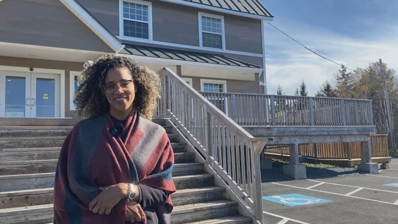 A Black woman in glasses wearing a shawl in front of a home