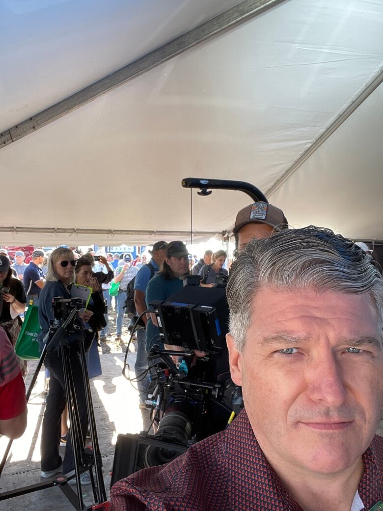 A man snaps a selfie in a tent at a farm progress show. 