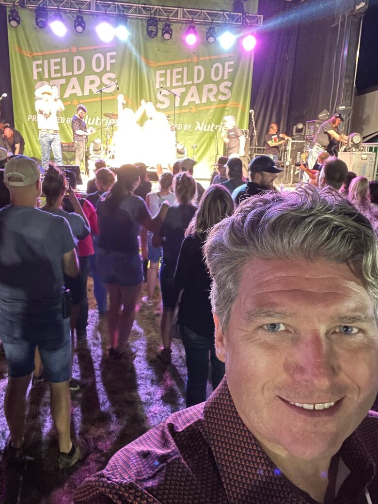 A man snaps a selfie in front of a stage a Stars Ambulance fundraising event. The banner on the stage says 