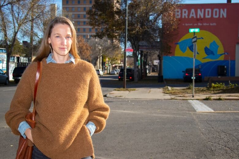 A women in a cozy brown sweater stands in front of a colourful mural.