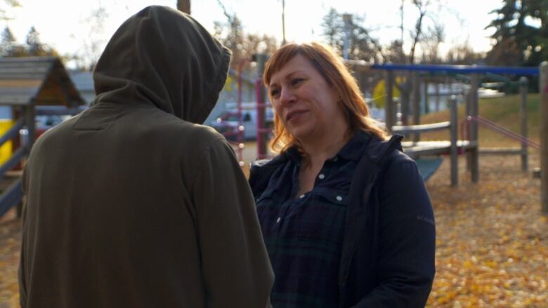 A woman with red hair speaks to a teenage boy whose face cannot be seen.