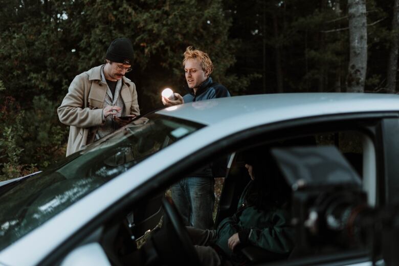 Two young people hold a light in front of a parked car.