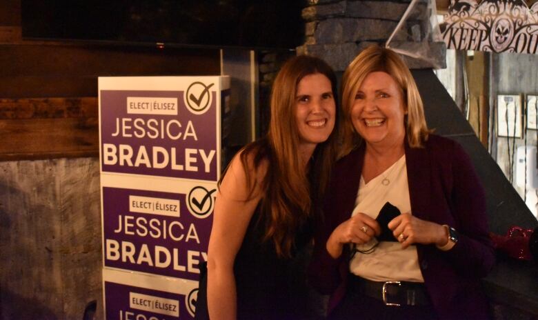 Two women pose next to an election sign.