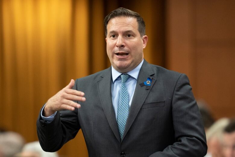 A man in a grey suit with a blue shift and a green tie stands.