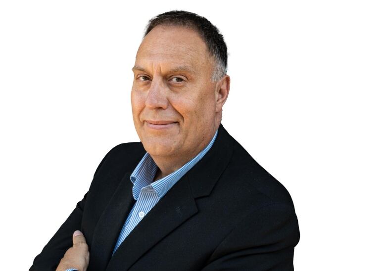 A man in a suit poses with his arms crossed and smiles in a professional photo.