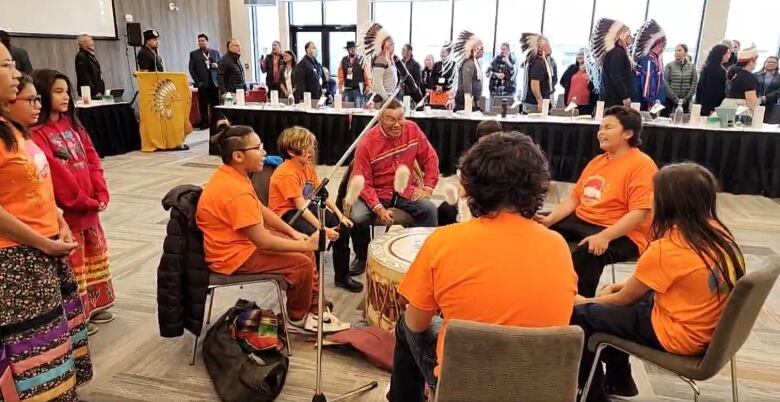 A group of young drummers in orange shirt sit in a circle.