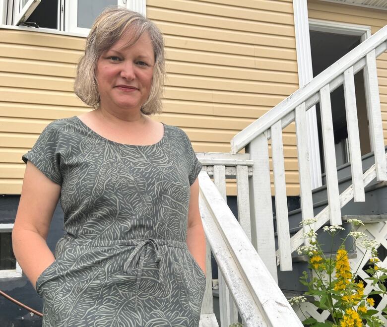 A woman stands on the front steps of a house.