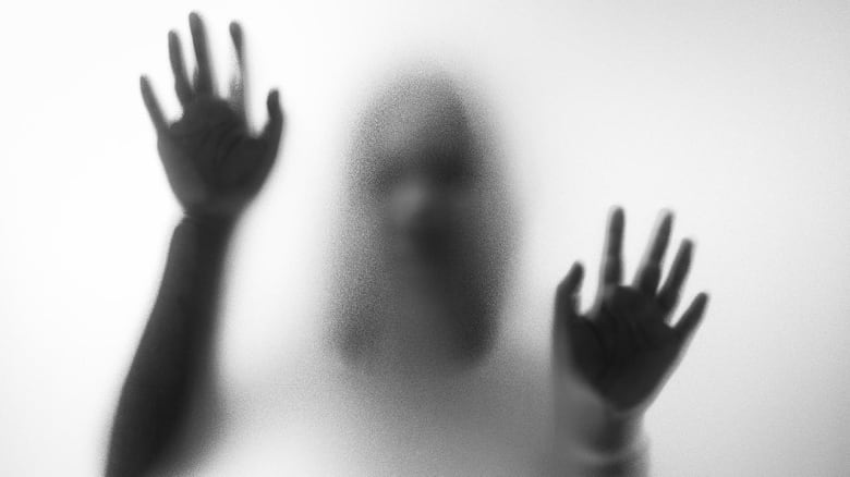 Blurry hands and body figure abstraction that looks like a ghost standing behind a glass pane with with her hands on it