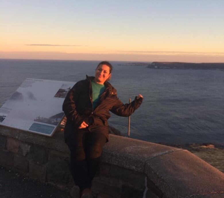 A woman poses on top of Signal Hill with the ocean in the background.