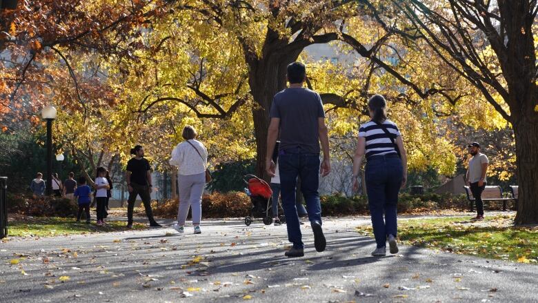 People walk on a path in a park on a sunny autumn day.