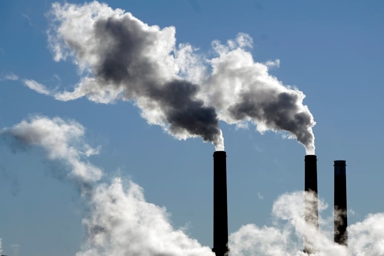 Three smokestacks belch smoke into a blue sky.