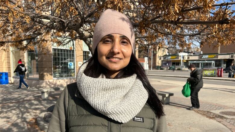 A woman wearing a toque, scarf and vest is smiling at the camera.