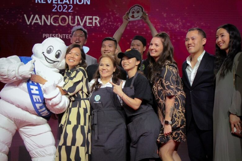 A group of nine people celebrate at the Michelin Guide awards, with one of them hugging a person dressed as the Michelin Man.