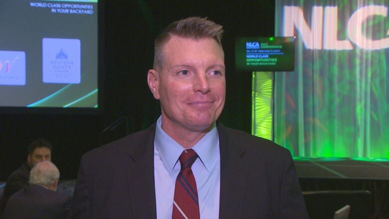 A man with his hair gelled into a faux hawk stands with a smile on his face at a business presentation.