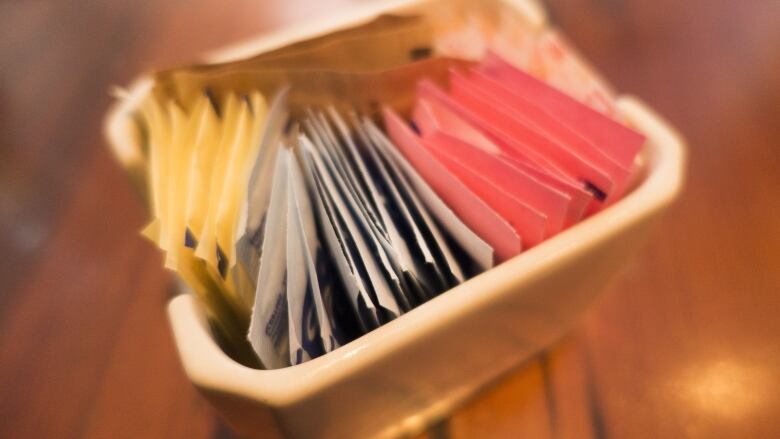 Several sugar and artificial sweetener packets sit in a dish on a table