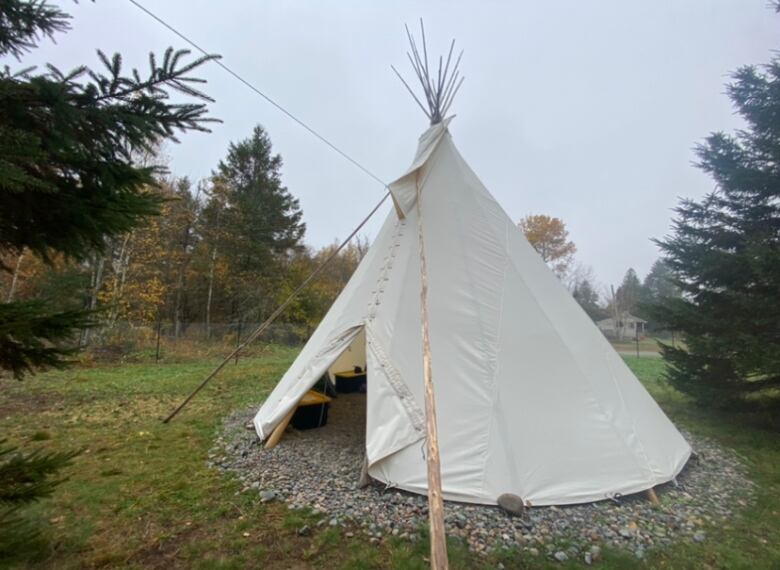 A white teepee sits outside surrounded by trees.