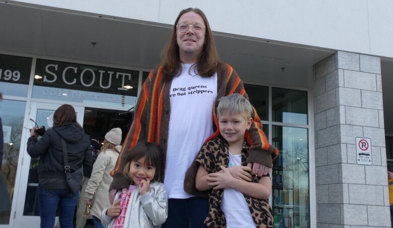 A smiling man stands with his arms around two smiling young children.